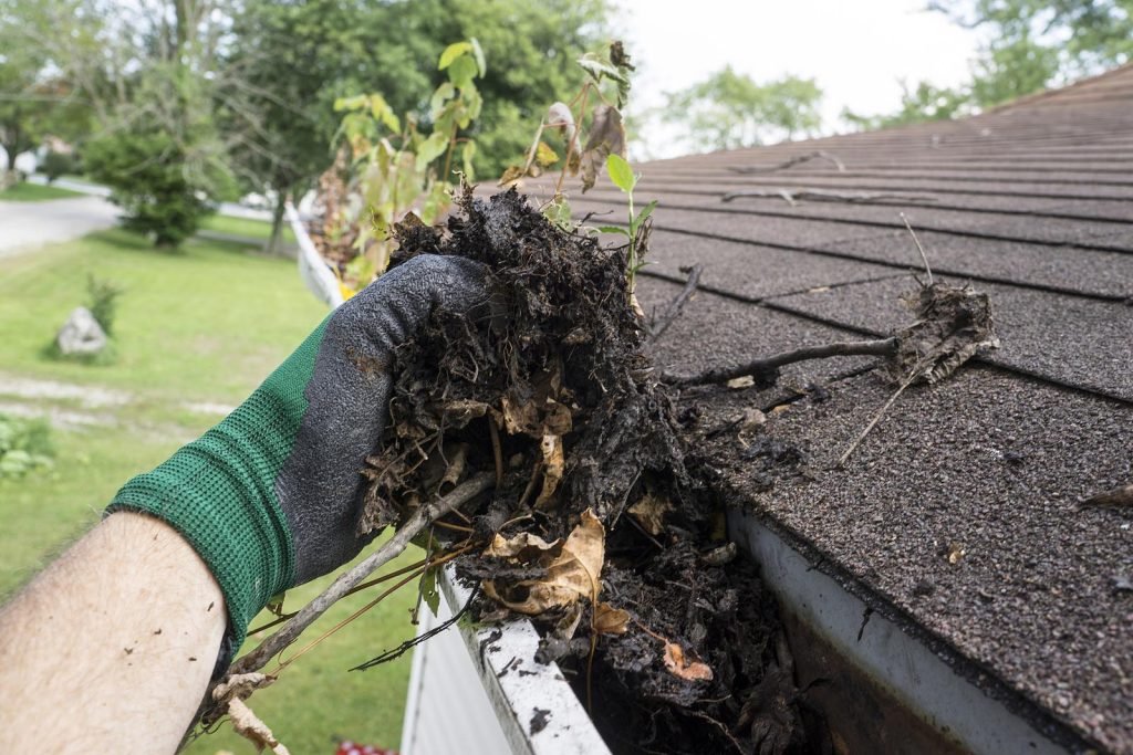 Worker cleaning gutters on a house as part of gutter maintenance.